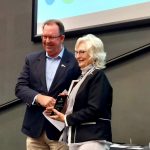 Stuart Coward shakes hands with Linda Ritchie as she accepts her award and smiles for the camera