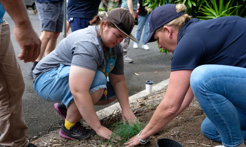 A participant and trainer kneel beside a garden bed, working together to plant greenery during an outdoor learning activity at STEPS Pathways College.