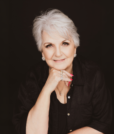 Portrait of Carmel Crouch against a dark background, resting her chin on her hand and facing the camera.