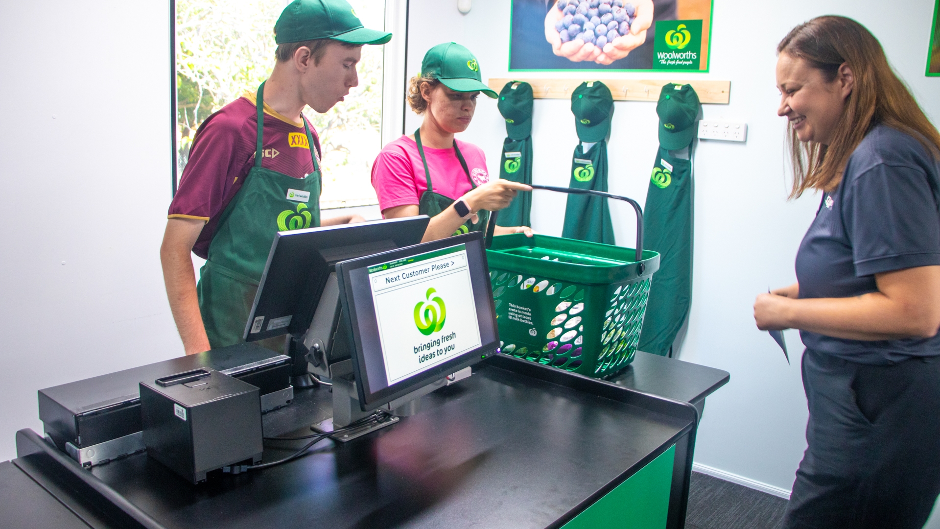 STEPS Pathways College students stand behind Mini Woolies counter and Point Of Sale (POS) System, practicing serving pretend customer.