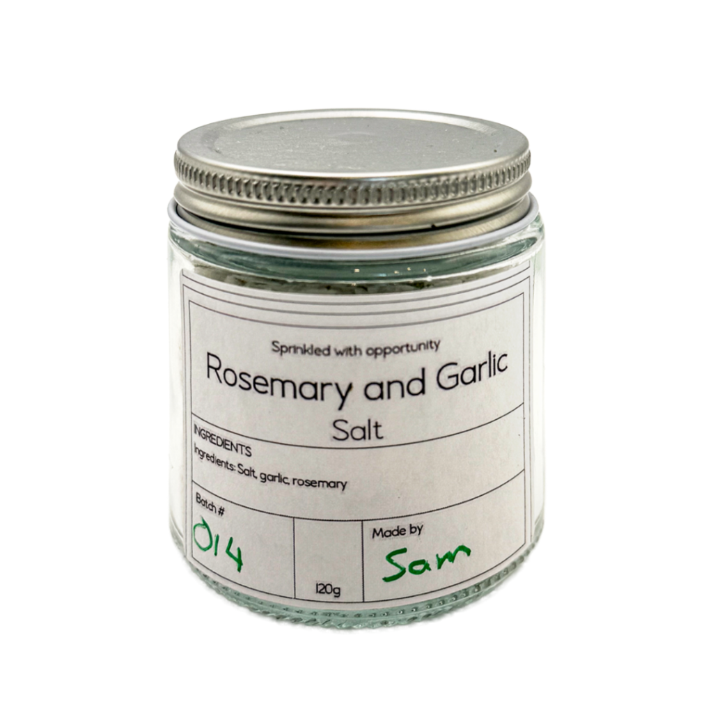 Glass jar of rosemary and garlic salt with a silver lid and product label, showcasing an artisan seasoning created through the Pathways to Plate program.