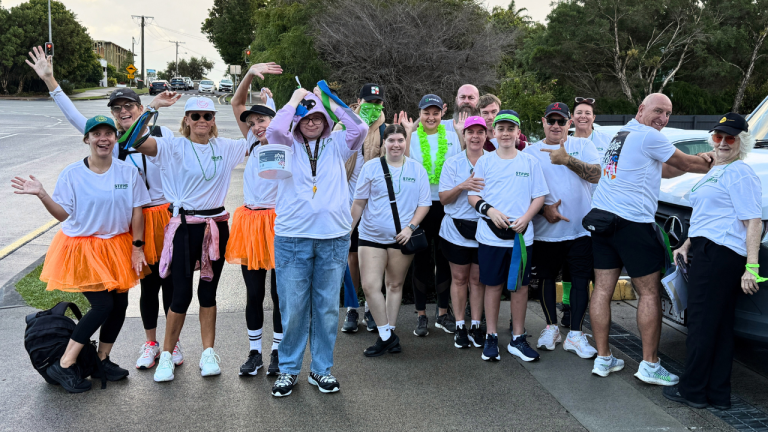 A group of people in matching ‘Steps for STEPS’ shirts smile and pose for camera.