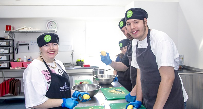 The STEPS Café on George kitchen full of staff and participants preparing food while smiling.