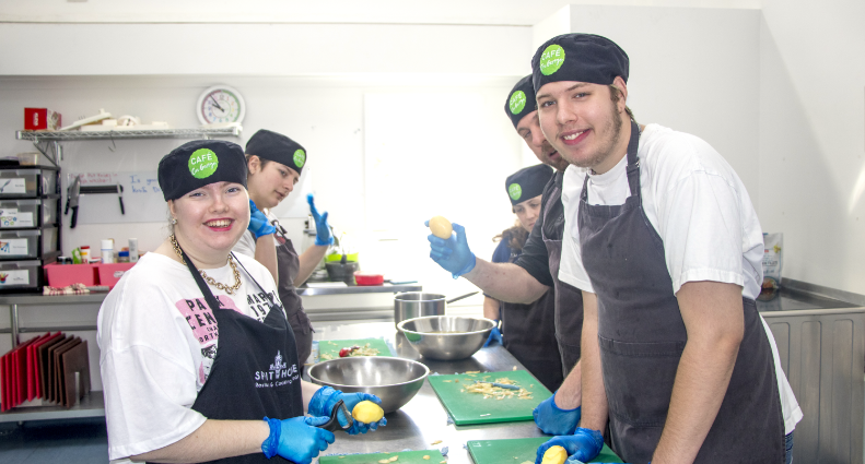 The STEPS Café on George kitchen full of staff and participants preparing food while smiling.