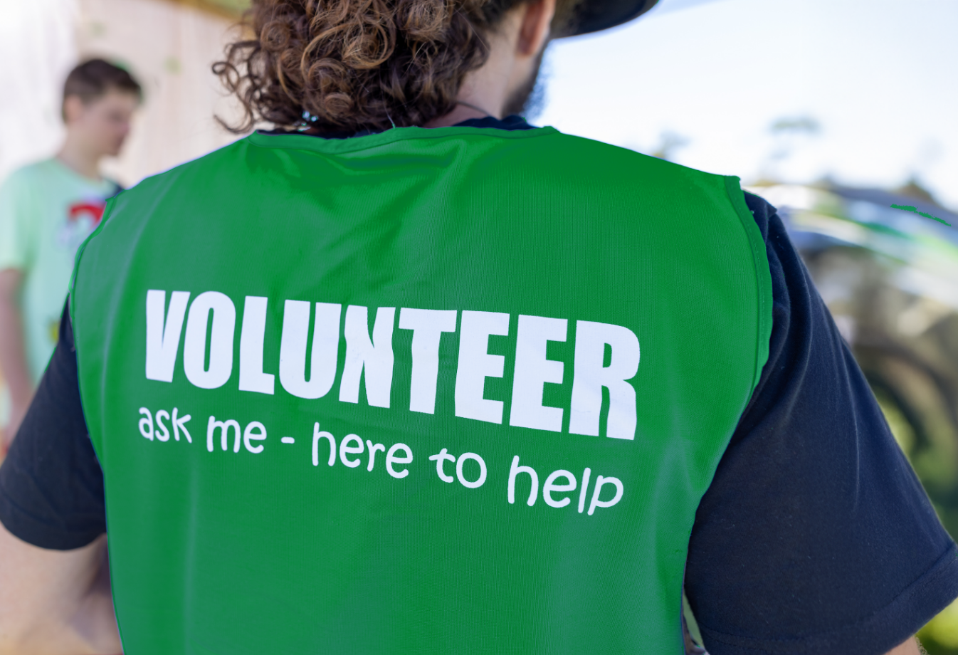 A green vest worn by a STEPS volunteer with the text 'VOLUNTEER. ask me - here to help'.